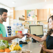 Smiling female cashier with buyer at checkout counter in grocery store