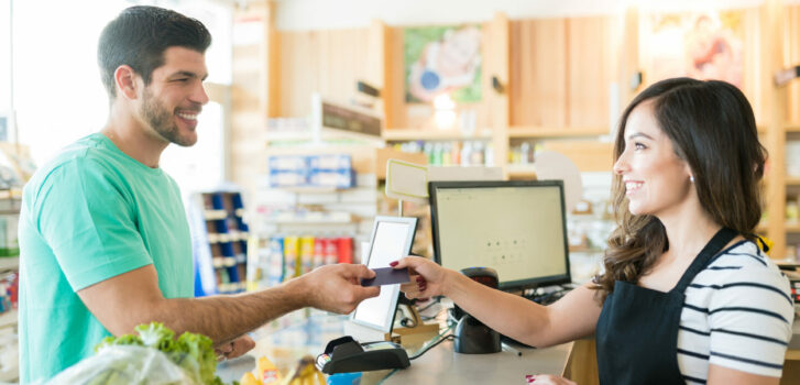 Man Making Payment Through Credit Card In Supermarket Smiling female cashier with buyer at checkout counter in grocery store